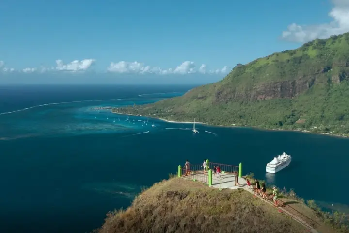 Tourists on a scenic overlook with a cruise ship in a bay surrounded by mountains and ocean