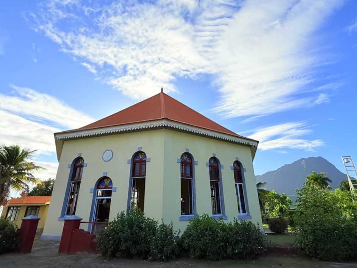 Octagonal building with red roof, arched windows, and lush plants against a blue sky.