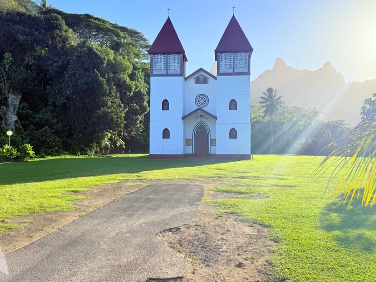 A white church with two red-roofed towers in a lush, sunny landscape.
