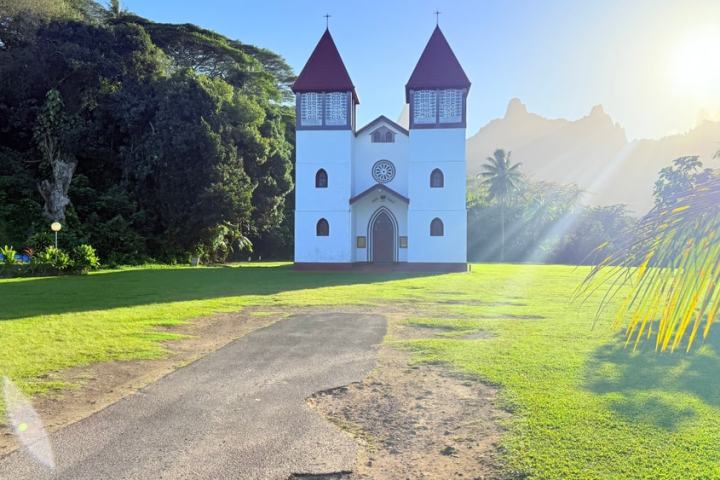 A white church with two red-roofed towers in a lush, sunny landscape.