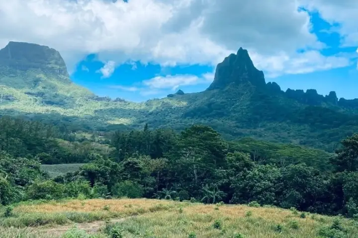 Lush green landscape with mountains and a partly cloudy sky.