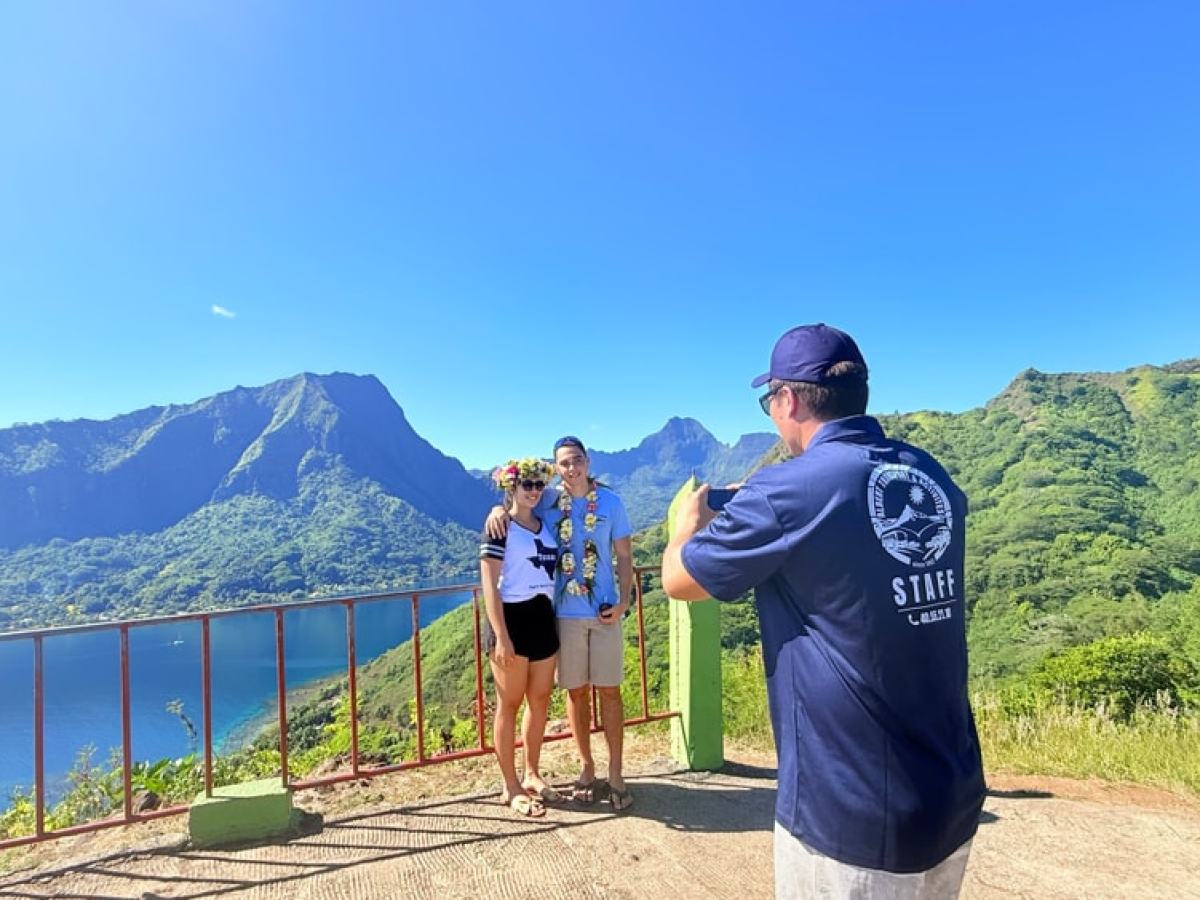 Two people pose for a photo with a stunning mountain and ocean view in the background.
