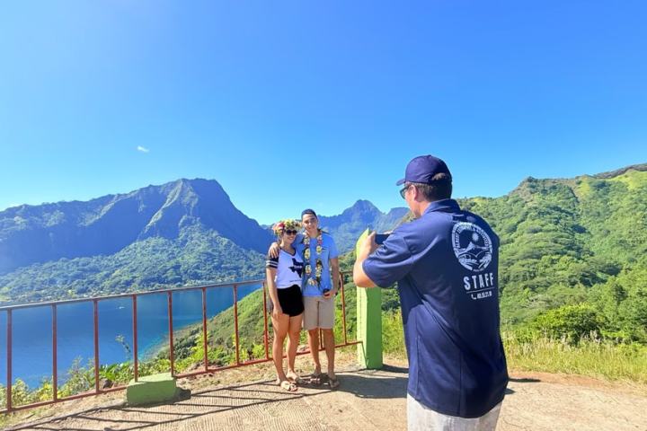 Two people pose for a photo with a stunning mountain and ocean view in the background.