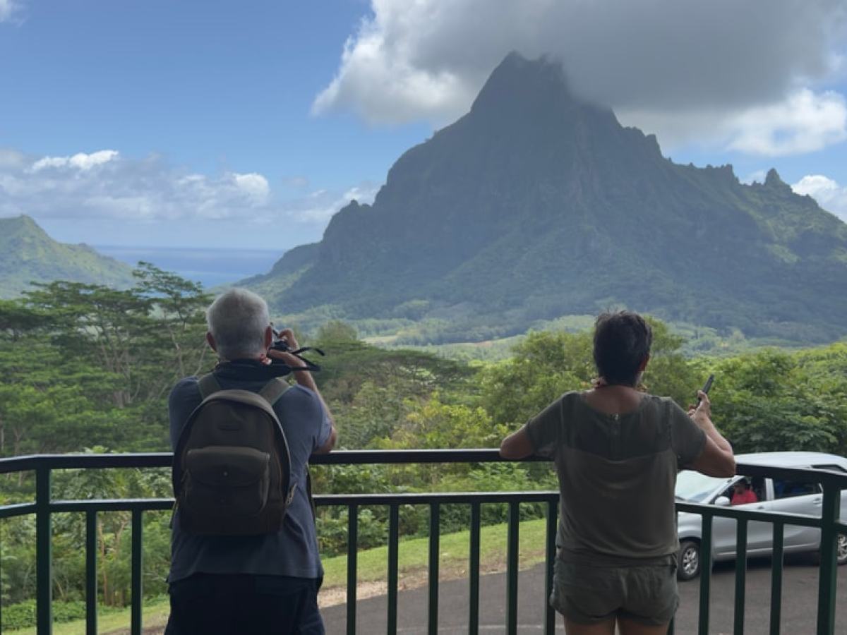 Two people taking photos of a mountain covered in clouds.