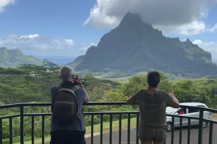 Two people taking photos of a mountain covered in clouds.